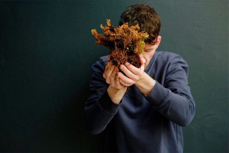 Photograph of a man holding furze from a bog in front of his face.