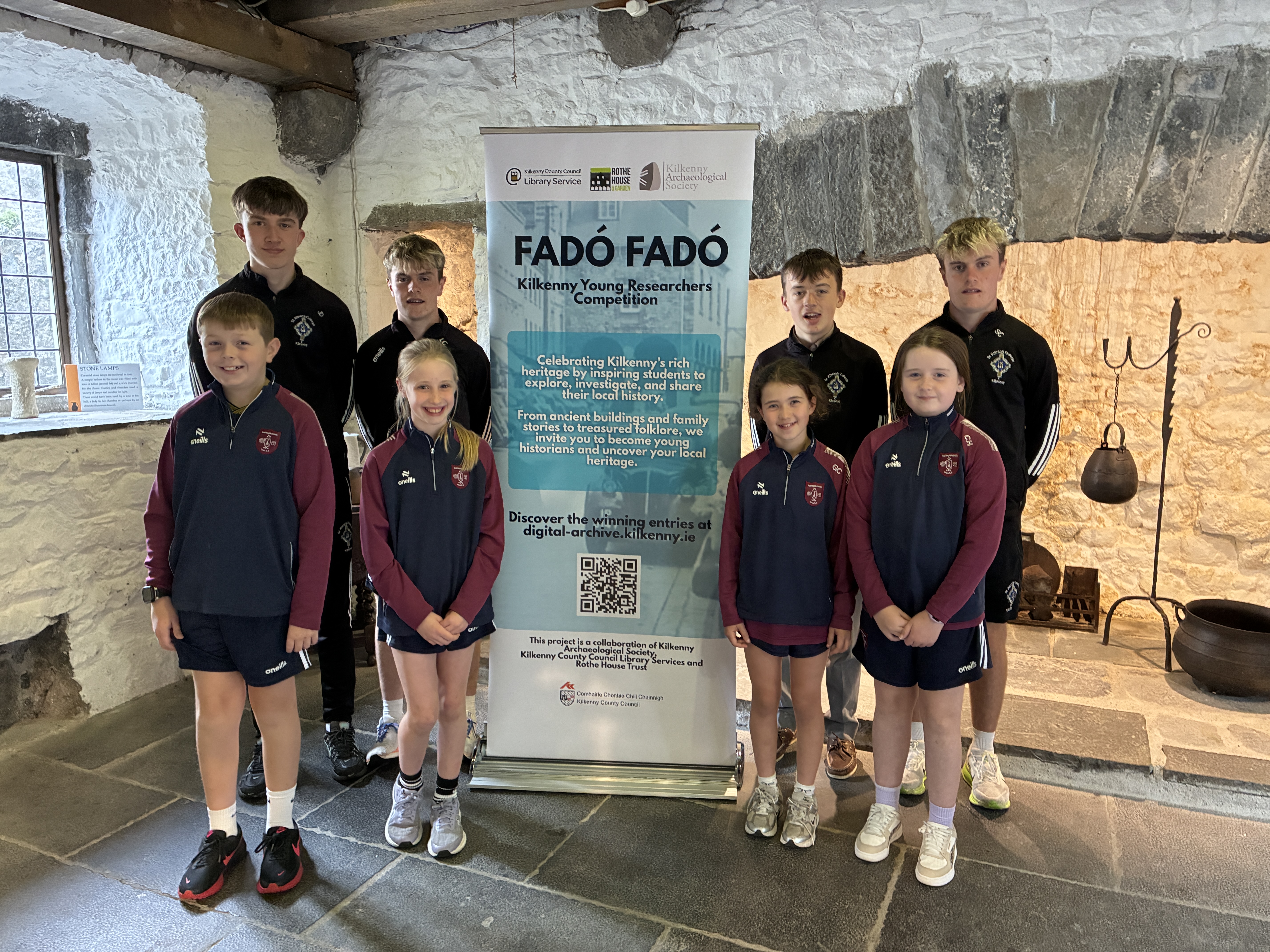 Fadó Fadó Launch 2027. Eight children stand around a pop-up banner for the Fadó Fadó competition in Rothe House.