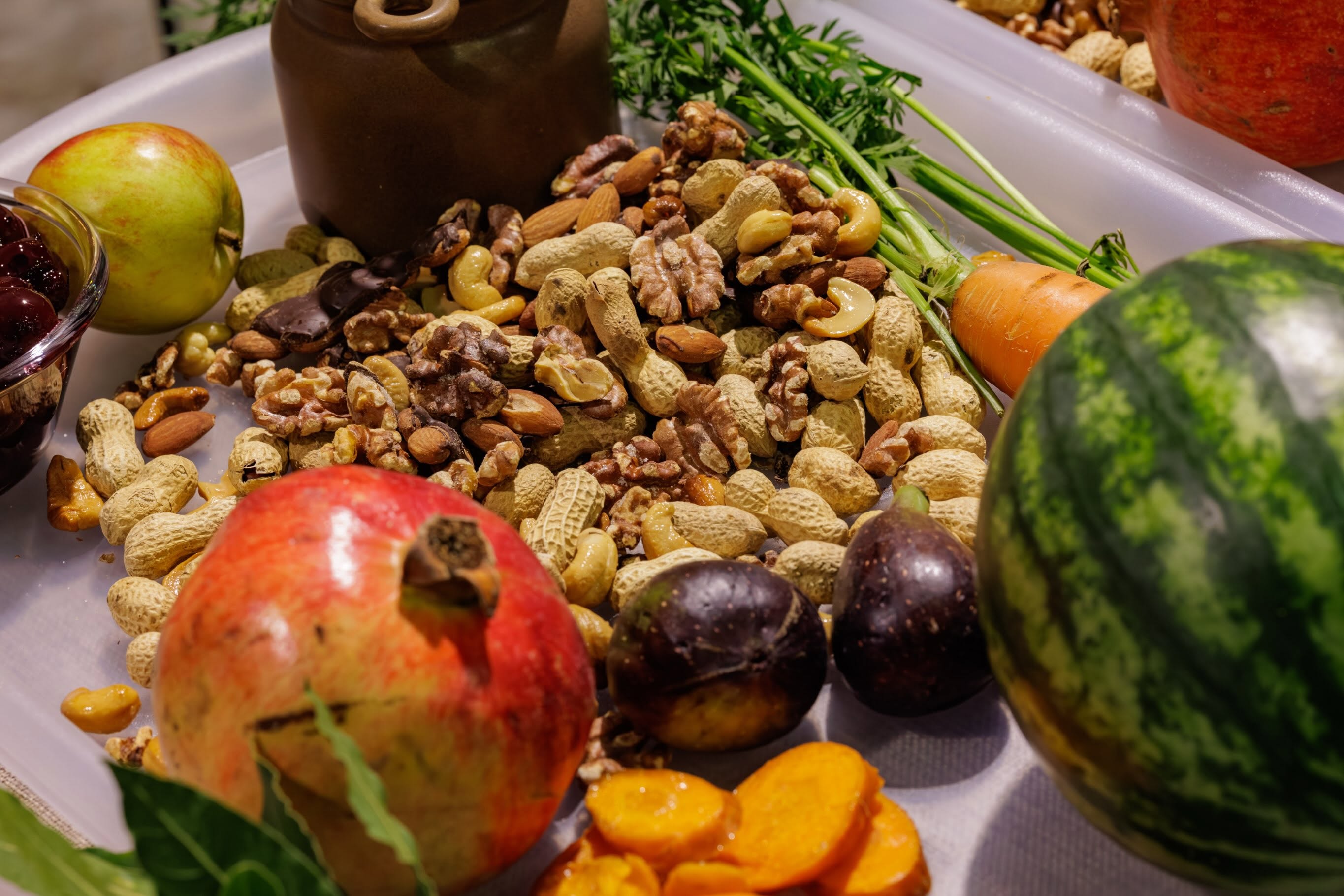 A close up of nuts and fruits from Savour Kilkenny's Medieval Banquet in Rothe House in 2025. A watermelon, monkey nuts, cashew nuts, carrots, apples, walnuts, and other produce.