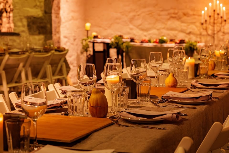 The Medieval Banquet at Rothe House during Savour Kilkenny 2025. A long table set for a formal meal with candles on the table. A warm atmosphere with orange candlelight in a medieval setting.